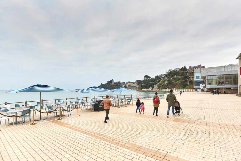 Un couple avec ses enfants se balade sur la digue de l'Ecluse à Dinard, en Bretagne. La digue piétonne permet de se balade entre la mer, les cafés et bar et le Palais des Arts et des Festival. Une promenade adaptée à tous et facile d'accès.