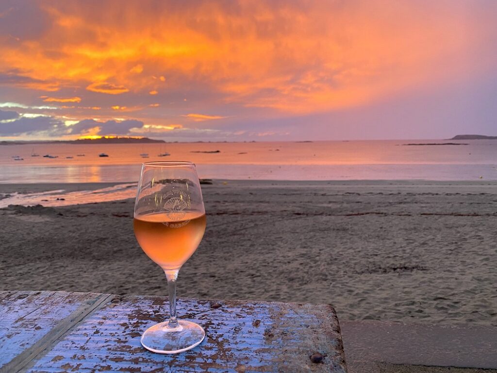 Coucher De Soleil Lancieux Sur Plage De Saint Sieu. Un verre de vin rosé est posé sur une table en bois à Kalypso La Cabane, restaurant de plage. La couleur du ciel ressemble à celle du verre de vin rosé.