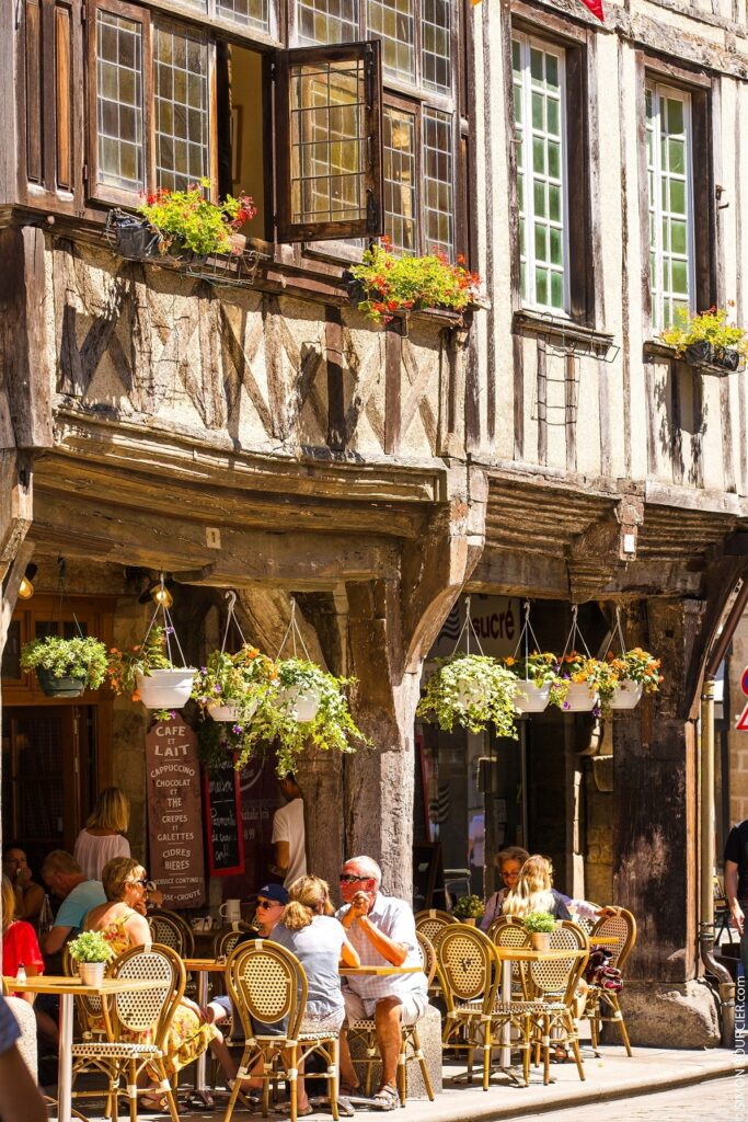 Des personnes sont installées en terrasse au rez-de-chaussée de maisons à colombages à Dinan, ville médiévale située à une vingtaine de kilomètres de Dinard.