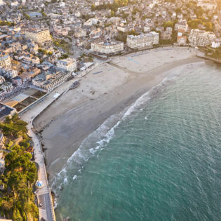 Vue aérienne de la Plage de l'Ecluse à Dinard. Joli contraste entre le bleu de l'eau et les batiments du centre-ville aux tons blanc des murs et gris des ardoises sur les toits.