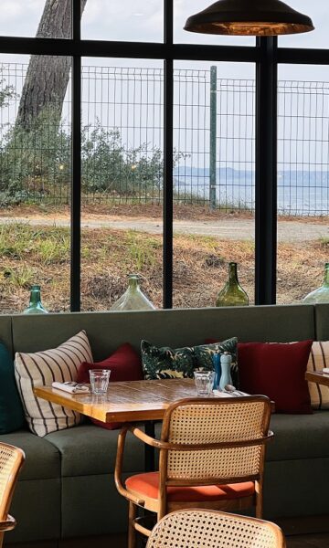 Tables, chaises et banquettes confortables avec des coussins colorés, disposés le long de grandes baies vitrées au Restaurant Du Nessay à Saint-Briac-sur-Mer. De l'intérieur du restaurant, le panorama s'ouvre sur la mer et le Cap Fréhel.