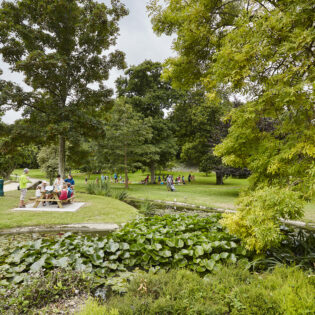 Une famille est attablée à une table de picnic au coeur du parc de Port Breton à Dinard. Ce grand espace vert est un parc public ouvert à tous et toute l'année. On peut profiter de jeux pour enfants, une roseraie, des arbres remarquables et un parc animalier. Le Parc de Port Breton est un des parcs et jardins remarquables de la côte d'émeraude.