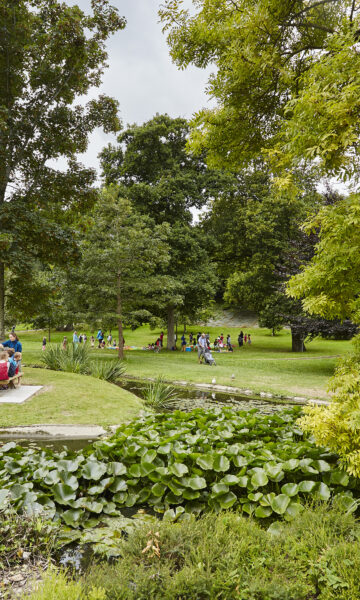 Une famille est attablée à une table de picnic au coeur du parc de Port Breton à Dinard. Ce grand espace vert est un parc public ouvert à tous et toute l'année. On peut profiter de jeux pour enfants, une roseraie, des arbres remarquables et un parc animalier. Le Parc de Port Breton est un des parcs et jardins remarquables de la côte d'émeraude.