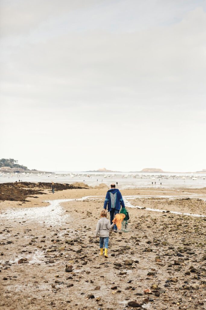 Un homme et un enfant arrivent sur la plage du Prieuré à Dinard à marée basse pour pratiquer la pêche à pied, activité nature récréative populaire en Bretagne et particulièrement appréciée lors des grandes marées.