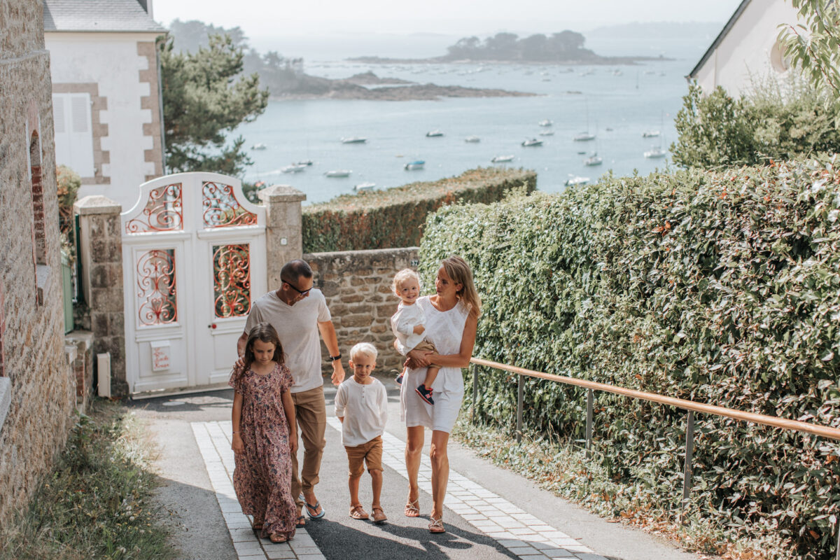 Une famille se promène sur le boulevard de la mer à Saint-Briac. Ils remontent la rue, et derrière eux, on peut apercevoir la mer étendu sous un ciel dégagé