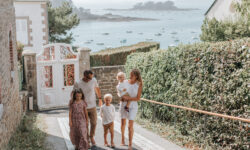 Une famille se promène sur le boulevard de la mer à Saint-Briac. Ils remontent la rue, et derrière eux, on peut apercevoir la mer étendu sous un ciel dégagé