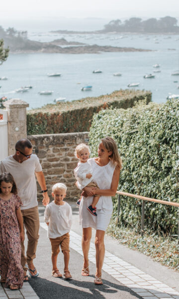 Une famille se promène sur le boulevard de la mer à Saint-Briac. Ils remontent la rue, et derrière eux, on peut apercevoir la mer étendu sous un ciel dégagé