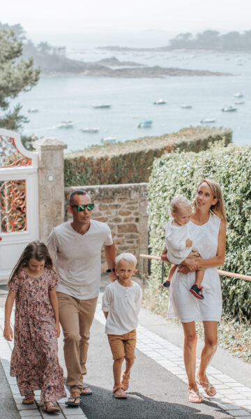 Un couple et ses trois enfants se promènent sur le boulevard de la mer à Saint-Briac. Ils remontent la rue, et derrière eux, on peut apercevoir la mer étendu sous un ciel dégagé