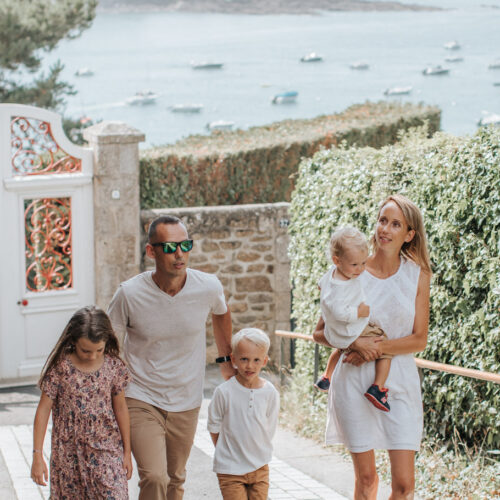 Un couple et ses trois enfants se promènent sur le boulevard de la mer à Saint-Briac. Ils remontent la rue, et derrière eux, on peut apercevoir la mer étendu sous un ciel dégagé