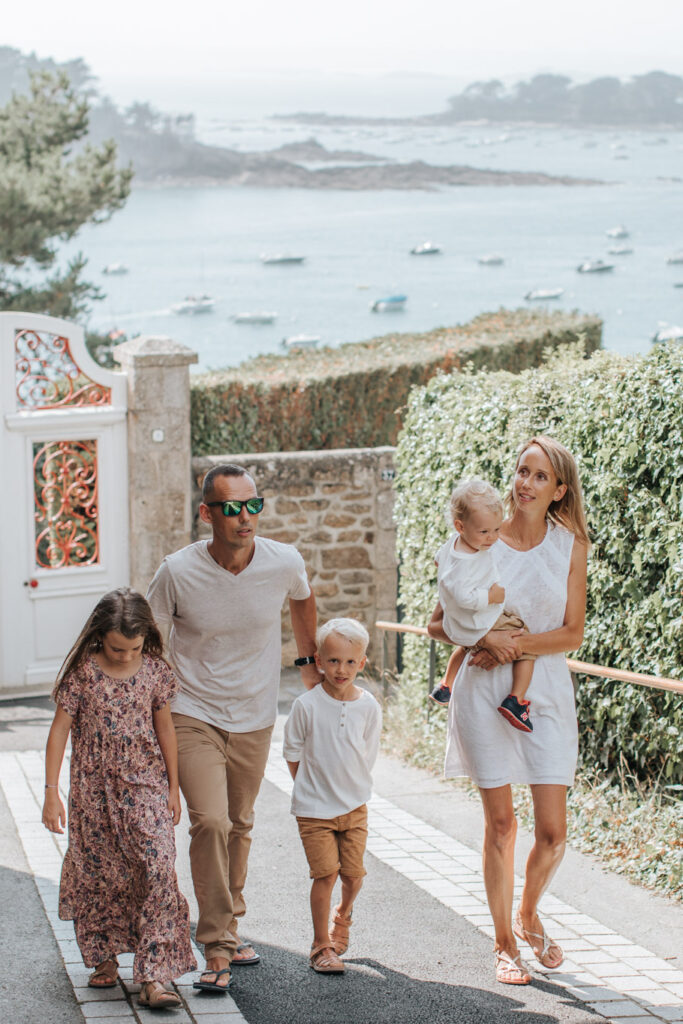 Un couple et ses trois enfants se promènent sur le boulevard de la mer à Saint-Briac. Ils remontent la rue, et derrière eux, on peut apercevoir la mer étendu sous un ciel dégagé