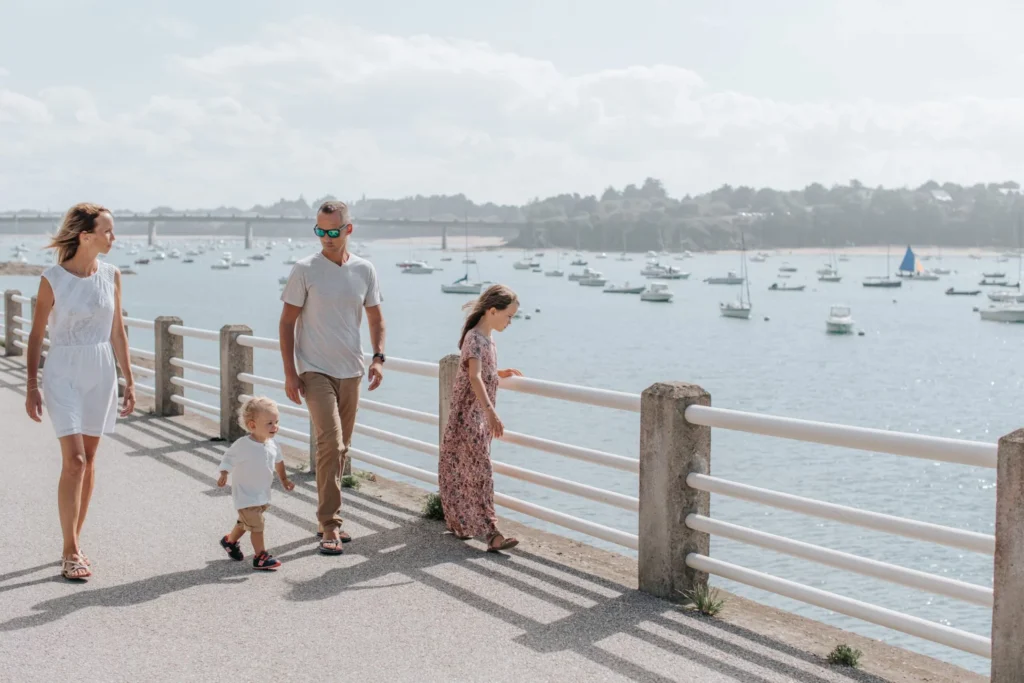 Une famille se promène avec ses trois enfants sur le Balcon d'Émeraude à Saint-Briac-sur-Mer, profitant d'une vue panoramique sur la mer scintillante sous un ciel clair