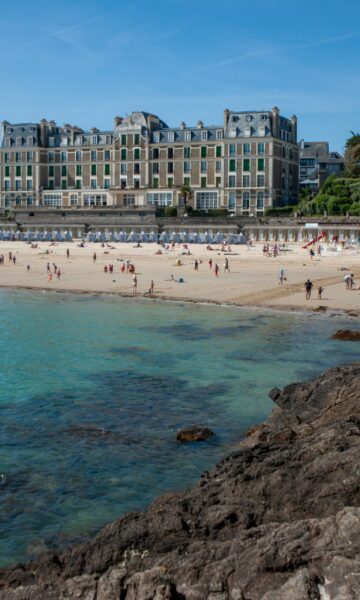 Un homme en sweat rouge court sur le gr34 de Dinard. Il s'agit de la pointe de la malouine, on aperçoit en arrière plan la plage de l'Écluse et le Royal.