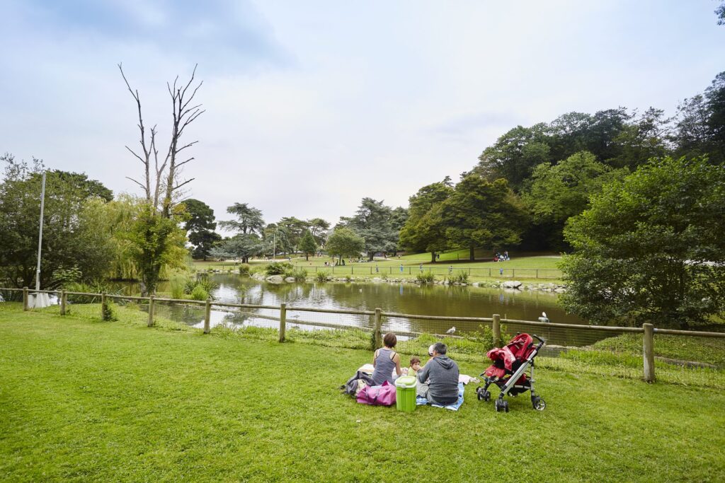 Une famille fait une pause dans le parc de Port Breton à Dinard. Ils se reposent près d'un sentier, entourés de verdure luxuriante, tandis que leur enfant repose tranquillement dans une poussette.