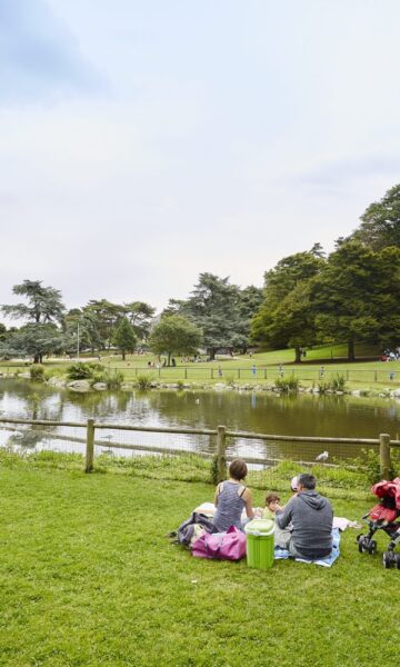 Une famille fait une pause dans le parc de Port Breton à Dinard. Ils se reposent près d'un sentier, entourés de verdure luxuriante, tandis que leur enfant repose tranquillement dans une poussette.