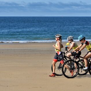 trois athlètes en pleine action durant l'Emeraude Tri Race sur la plage de Longchamp, concentré et dynamique, reflétant l'esprit sportif et la détermination face à l'épreuve.