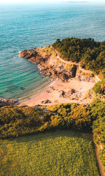 Vue d'une jolie crique à Dinard, sur la Côte d'Émeraude au coucher du soleil. La végétatiton surplombe la plage de sable fin.