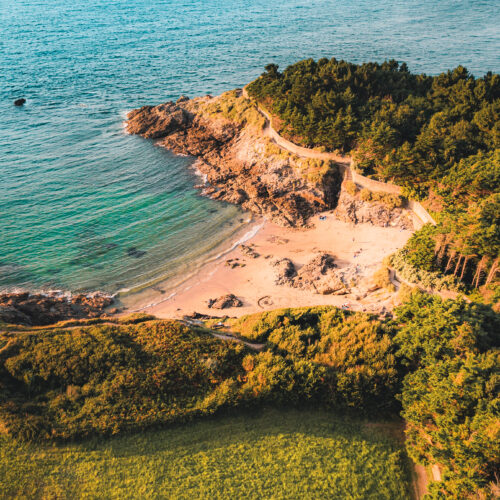 Vue d'une jolie crique à Dinard, sur la Côte d'Émeraude au coucher du soleil. La végétatiton surplombe la plage de sable fin.