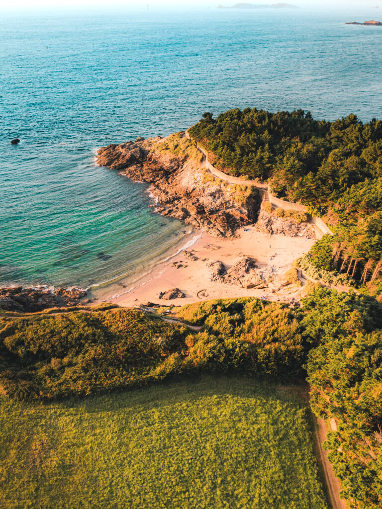 Vue d'une jolie crique à Dinard, sur la Côte d'Émeraude au coucher du soleil. La végétatiton surplombe la plage de sable fin.