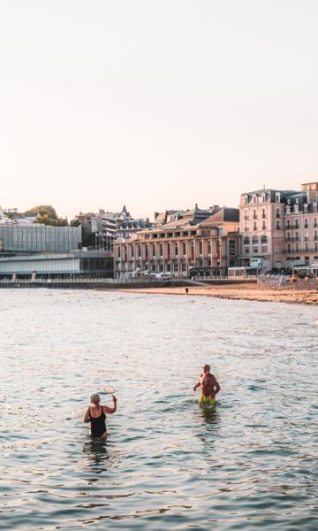 Sur la Plage de l'Écluse à Dinard, un couple de retraités se baigne dans la mer sous une lumière douce de début de journée. La lumière matinale teinte l'environnement de couleurs pastel, et le calme de la mer ajoute une sérénité à l'atmosphère. Le couple, en pleine baignade, semble apprécier ce moment paisible, entouré par la beauté naturelle de la plage au lever du soleil.