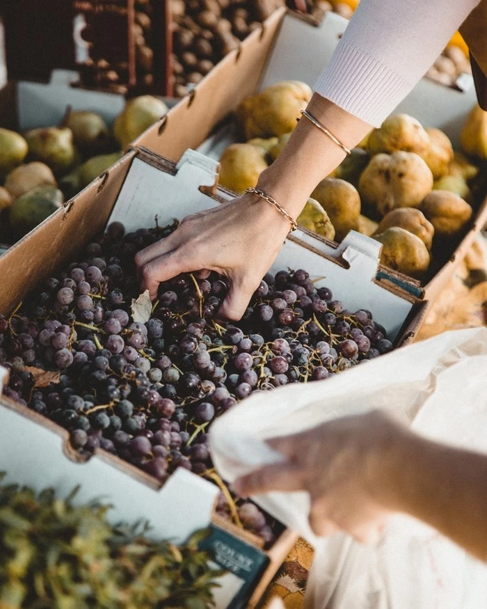 Les marchés et brocantes de la Côte d'Émeraude. Stand de fruits et légumes. Une personne se sert en raisins noirs sur le marché.