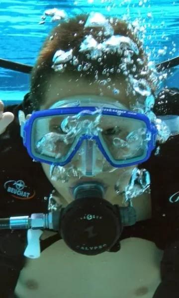 Un plongeur fait un signe sous l'eau dans une piscine. Apprenez la plongée avec Nautilus Dive Center à Dinard et participez à des sorties de Plongée Sous Marine en Bretagne.