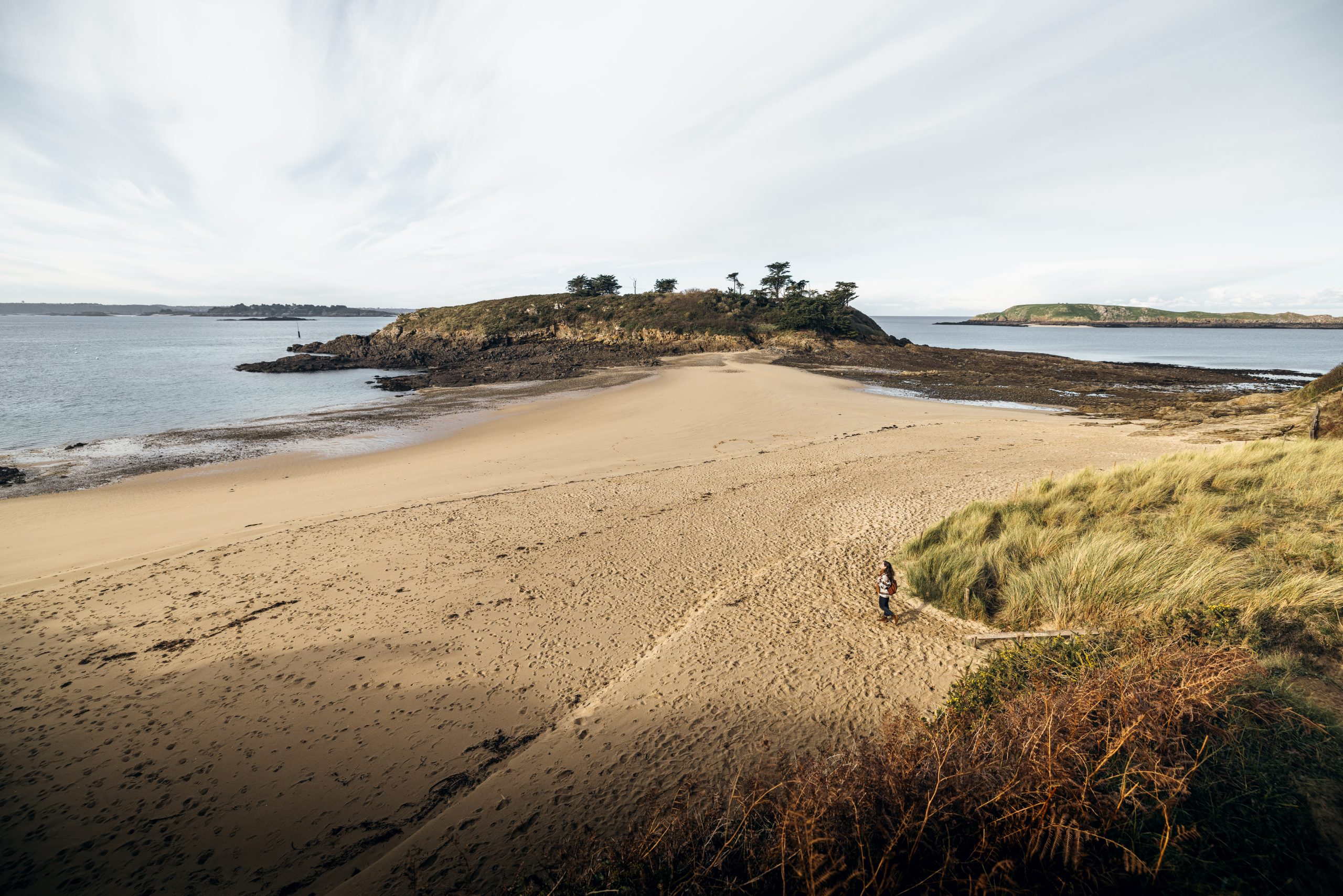 Photo de la Plage Du Perron à Saint Briac sur Mer. Cette plage est reliée à un îlot par un tombolo découvert à marée basse. Cette petite crique intimiste sur la côte d'Emeraude est idéale pour se baigner et profiter des rayons du soleil en toute tranquilité.