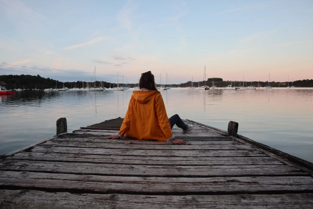 Ponton de la cale de Montmarin à Pleurtuit. Une femme assise sur le ponton observe le coucher de soleil avec ses nuances de bleu et de rose. Elle porte un ciré jaune. 