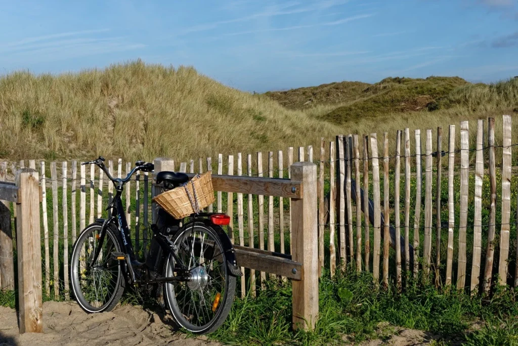 Un vélo est attaché à une barrière en bois, le long de dunes sableuses sur la Côte d'Émeraude. (c) Frank Hamel