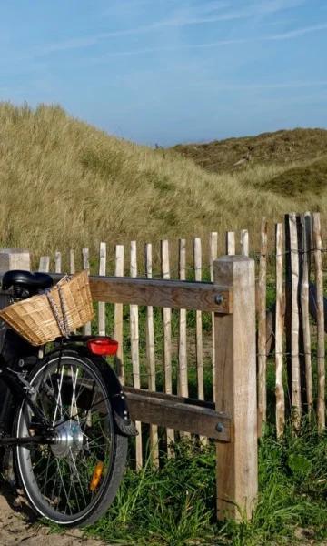 Un vélo est attaché à une barrière en bois, le long de dunes sableuses sur la Côte d'Émeraude.