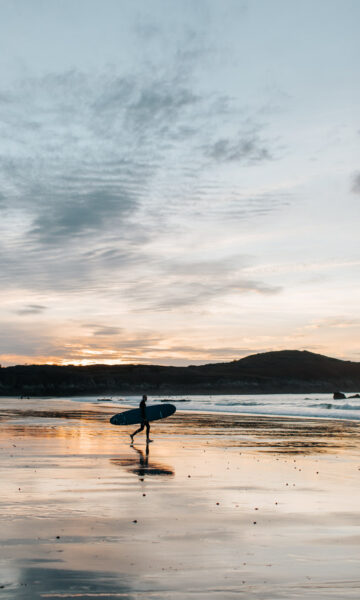 Un surfeur se dirige vers la mer au coucher du soleil sur la plage de Longchamp, spot de surf de la côte nord de la Bretagne, située sur les communes de Saint-Lunaire et Saint-Briac-sur-Mer.