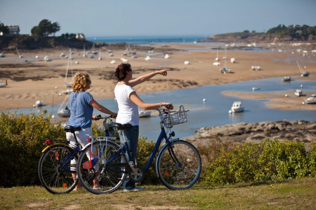 Deux femmes sont posées à côté de leurs vélos sur le balcon d'Emeraude à Saint-Briac-sur-Mer. Elles regardent la cale du Béchet à marée basse.