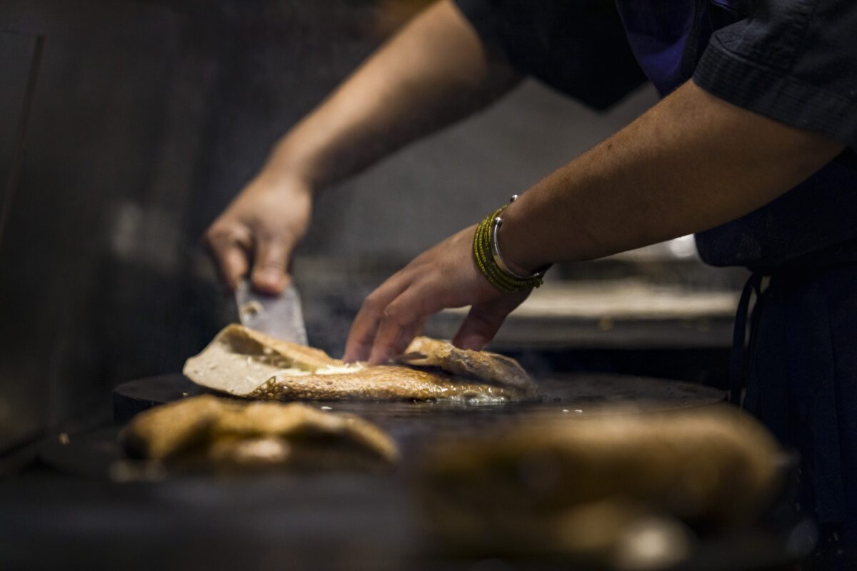 Un maître crêpier cuisine une galette de sarrasin. la photo zoom sur ses mains.