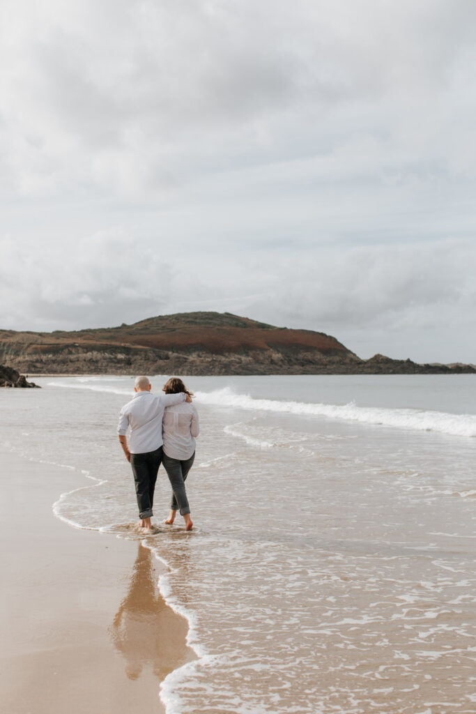 Scène romantique. Un couple marche sur la plage de Longchamp à Saint-Lunaire les pieds dans l'eau.