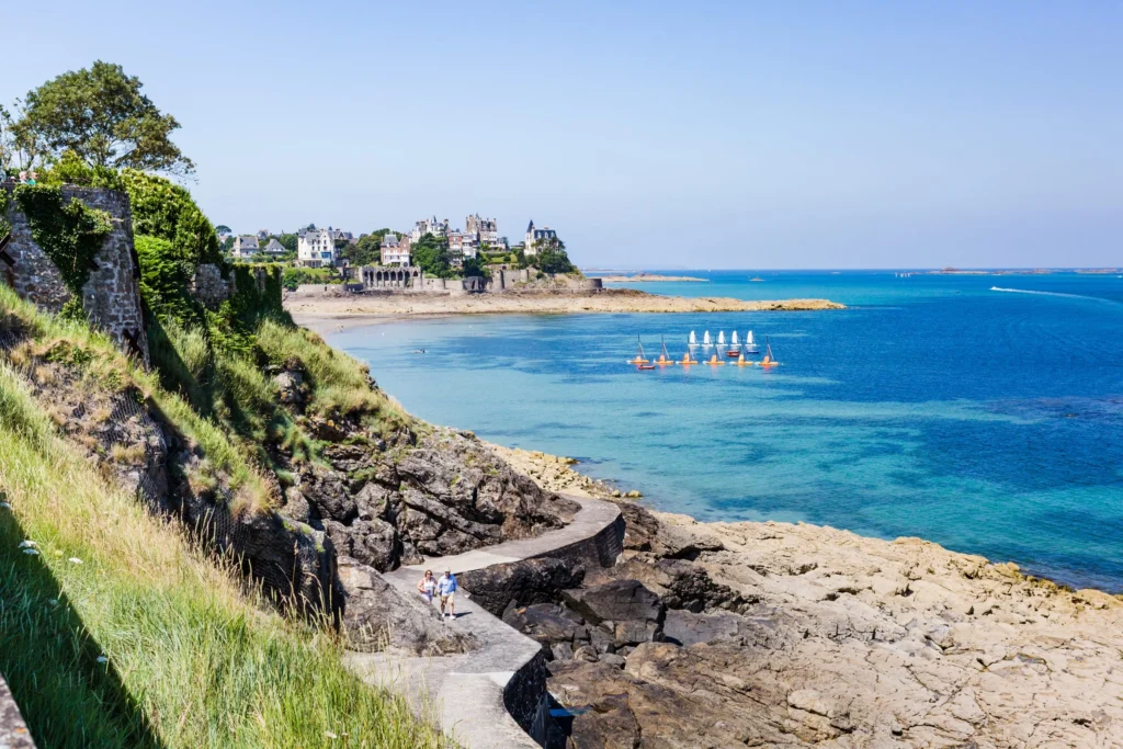 Dinard par Alexandre Lamoureux. Le gr34 qui longe la mer. On aperçoit la pointe de la Malouine en fond et les bateaux à voiles sur l'eau. 