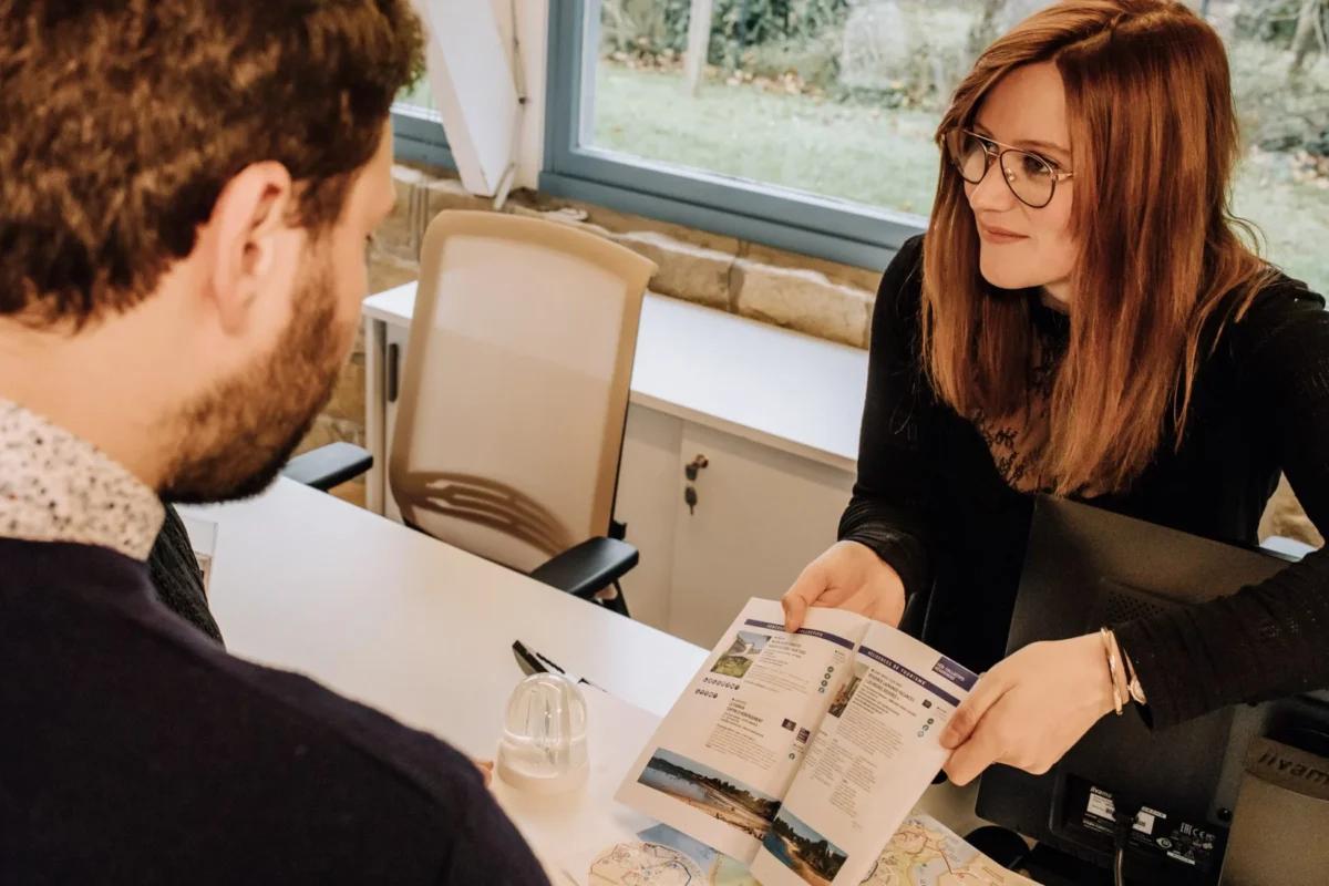 Une conseillère en séjour présente l'offre touristiques à un touriste. elle est dans le bureau d'information tourisme de Lancieux