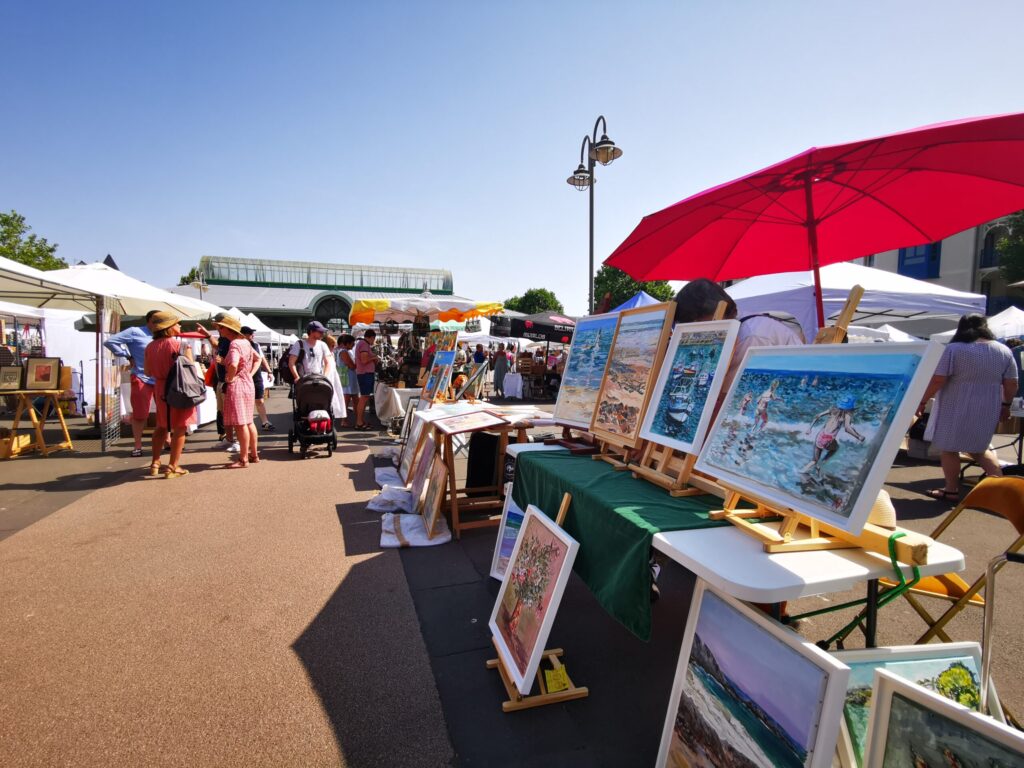 Des tableaux sont exposés au Marché Dinardais De La Création organisé sur l'esplanade de la Halle à Dinard. Visitez les marchés de créateurs de la Côte d'Émeraude. Crédit Ville De Dinard